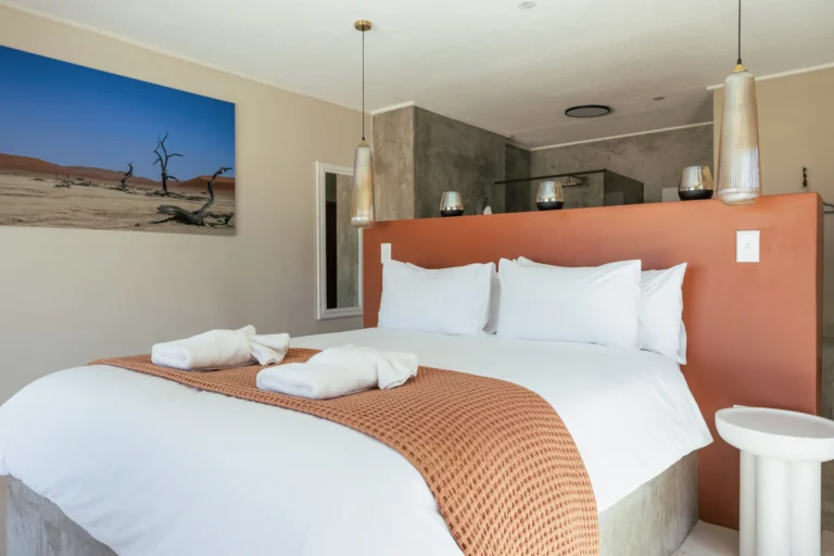 Modern desert-inspired bedroom featuring a terracotta orange headboard, white bedding with a rust-colored throw, and a large Deadvlei landscape wall art print.