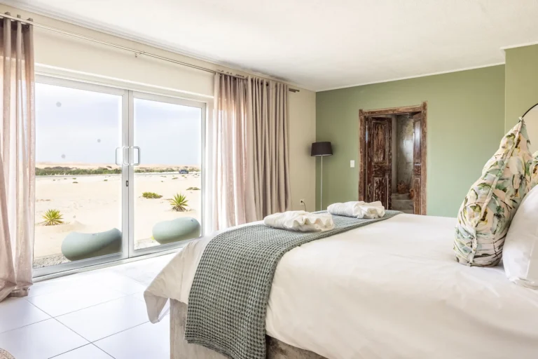Bright modern bedroom featuring a sage green accent wall, rustic wooden door, and sliding glass doors overlooking a desert landscape.